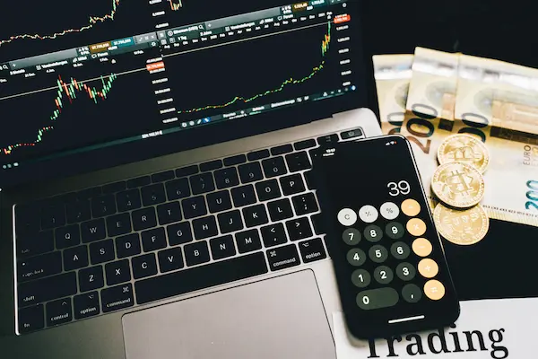 Pantalla de trading con gráficos financieros y billetes de dólar sobre una mesa, representando una cuenta fondeada operando con capital externo